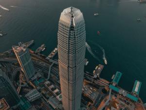 The Two International Finance Centre skyscraper towering over the dense urban skyline of Hong Kong's financial district, set against a mountainous backdrop.
