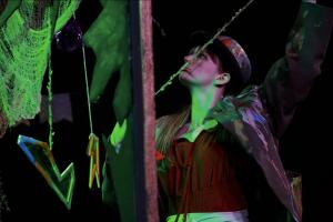 A performer stands beneath green stage lighting amid the surreal set of The Inverted Realm.