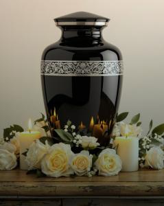 Black memorial urn with silver detailing surrounded by white roses and candles.