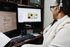 Natasha Broxton working at a computer with dual monitors while using business systems for government-contracting research and preparation.