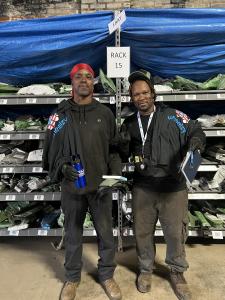 Two Select Auto Parts team members standing in front of labeled auto-parts inventory racks.