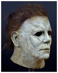Michael Myers Maske im Stil von Halloween (2018): verwittertes, cremeweißes Latexfinish mit eingearbeiteten braunen Haaren, gezeigt im Halbprofil.