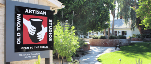 Sign for Old Town Artisan Studios with a garden pathway and trees leading to a white house in the background.