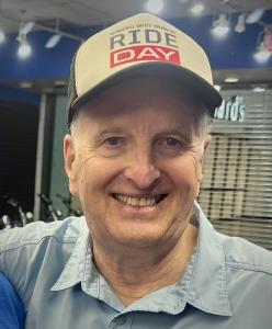 A close-up photo of Dr. Ray Ochs's face. He is wearing a ballcap with the words RIDE Day on it and is smiling. He is wearing a blue collared shirt.