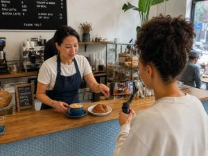 A creator filming coffee and pastries on a phone gimbal while a café owner sets them on the counter.
