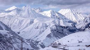 Panoramic view of snow-covered Caucasus Mountains and a winding mountain road in Gudauri, Georgia.