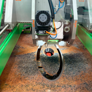 Close-up of a CNC machine milling an angled 45-degree oval cable penetration hole in a steel shell surrounded by metal shavings.