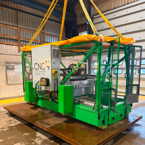 A green CNC Onsite 4-axis gantry milling machine suspended by yellow crane lifting straps inside an industrial workshop.