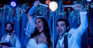 Bride and groom actors lighting a candle in a production of Tony n' Tina's Wedding, returning to The Rio Hotel & Casino in August 2026.