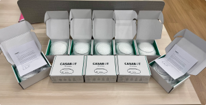 Rows of open white CASABOT CB-Gateway retail boxes on a wooden table, each containing a bubble-wrapped device, with printed and signed letters placed inside two of the boxes.