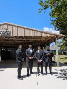 4 key TDCG members in black suits and faces blurred stand for a photo.