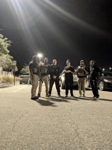 Several TDCG Members stand in the street in the night, donning their tactical gear
