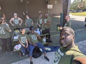Several people of all types all wear Fishhawk Chamber of Commerce dark green shirts with white names of sponsors and the event itself.