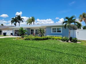 Landscaped Florida front yard with green lawn, tropical plants, flower beds and palm trees in front of a home.