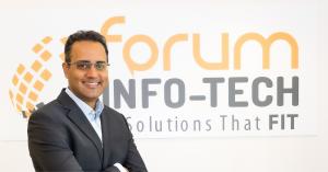 Biren Shukla, Founder and CEO of Forum Info-Tech, standing in front of the Forum Info-Tech logo