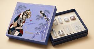 An open Naru Ham sample box from Hannaru, its lid decorated with a mother-of-pearl najeon tiger and magpie and the line Meet Rising K-Beauty, holding retail-size Korean cosmetics samples arranged in a fitted cream insert.