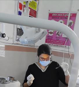 Dr. Praisey Thomas, née Yesudas, Dentist and Medical Officer, working in the clinical operatory at Dr. Shyama Prasad Mukherjee Civil Hospital (also known locally as Sarkari Aspatal), wearing a face mask, protective glasses, and surgical gloves while handl