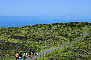 Hikers cross the lava fields on the Mt. Mihara crater trail, Izu Oshima, with the sea and a distant Mt. Fuji beyond.