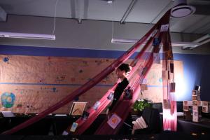 The image depicts the artists and researcher Mira Svilenova with the creative installation, including the Glagolitic work of 200 artists from global diasporic communities.