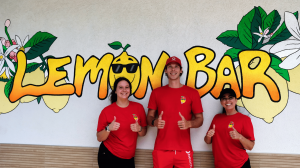 Casey Robson, Kate Mangan and a Lemon Bar team member stand smiling in front of the Lemon Bar mural in Neptune Beach, Florida.