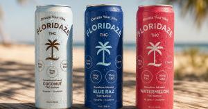 Three Floridaze THC seltzer cans in Coconut, Blue Raz and Watermelon standing on weathered wood at a Florida beach.