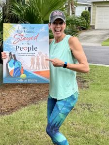 Author Colleen Riddle holding a poster of the book cover for Came for the Game, Stayed for the People.