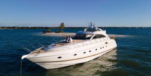 A white motor yacht anchored in calm blue water off a small Tampa Bay sandbar, with two guests seated on the bow deck under a clear sky.