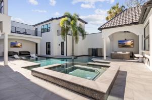 The courtyard of a modern white luxury estate with a swimming pool, sunken spa, covered lounge areas and a palm tree at the center.