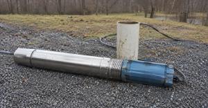 Submersible well pump and motor assembly lying on gravel beside an open well casing in a rural yard.