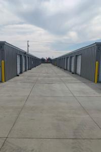 Wide outdoor drive-up aisle between rows of grey self-storage buildings at Freedom Storage Inc. in Visalia, California.