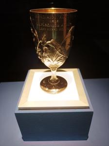 A close-up shot of the 1896 pure silver Bréal's Cup, a 15-centimeter-tall Olympic trophy featuring Art Nouveau reliefs of birds and plants from Marathon, Greece.