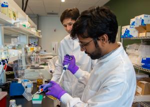 scientist in white lab coat pipetting sample into well