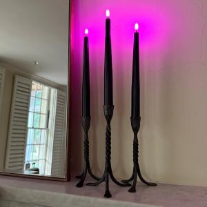 Celestial At Home black flameless Halloween wax taper candles switched to purple flame mode, glowing in twisted iron candlesticks against a purple-washed wall