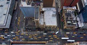 Aerial view straight down onto a busy NYC intersection, taken from an unguarded rooftop edge.