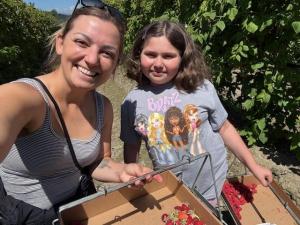 An adult woman and a young girl smiling together while picking berries at a farm, each holding a box of freshly picked berries.