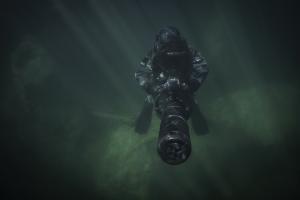 Technical diver operating an underwater propulsion vehicle in dark, low-visibility water.