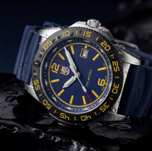 Close-up of a Luminox dive watch with a blue dial and rubber strap, yellow markers, stainless steel case and black dive bezel, covered in water droplets against a dark wet background.