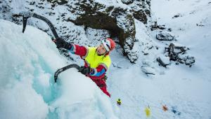 ICE SAR rescue climber using two ice axes while ascending a frozen waterfall in snowy mountain terrain.