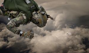 Military parachutist in tactical gear wearing a Luminox watch during a high-altitude jump above the clouds.