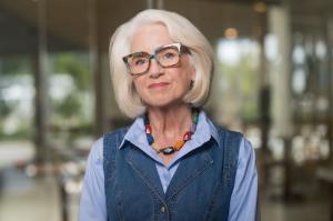 Tennessee psychotherapist Judy K. Herman wearing colorful glasses, a blue shirt and denim vest looking warmly at the camera.