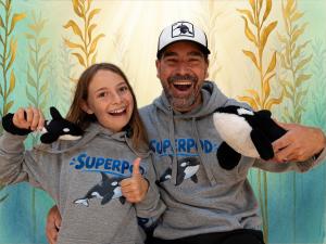 A father and daughter holding plush toy orcas