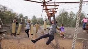 a boy reaches for rungs on a traverse element within an enclosed net for kids adventure course