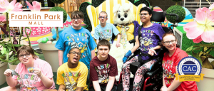 Group of smiling children wearing Easter-themed shirts posing with a person in a bunny costume at Franklin Park Mall.
