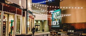 Outdoor nighttime view of Franklin Park Mall entrance with string lights, shoppers, benches, and a lit store sign.