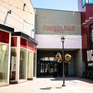 Entrance to Franklin Park Mall with storefronts, string lights overhead, and hanging flower baskets on a lamppost.