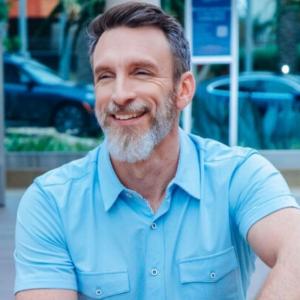 Portrait of Mike Michalowicz smiling in a light-blue short-sleeved shirt.