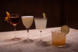 Four cocktails in assorted glassware on a marble table at Gunny’s Pub, including citrus-garnished drinks against a dark wood backdrop.