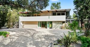 Exterior front view of a two-story mid-century modern house with mature landscaping and post and beam design