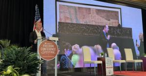 National World War I Memorial sculptor Sabin Howard speaks at the Steamboat Institute’s 18th Annual Freedom Conference in Beaver Creek, Colorado, with a projected image of Howard and his wife, producer and studio head Traci L. Slatton alongside imagery of