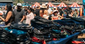 Stacks of backpacks ready for distribution as families and children gather at an outdoor community Back-to-School event.